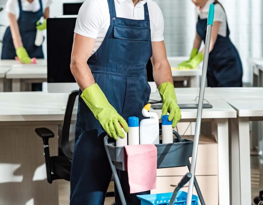 young-cleaner-standing-near-cart-with-cleaning-supplies.jpg